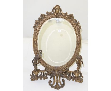 Mid 20th C decorative brass table mirror, oval shaped and bevelled with floral mounts, the base mounted with 2 cherub figures