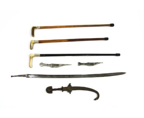 Three Eastern daggers in scabbards, a sword blade and three malacca walking sticks, the largest dagger with carved wooden han