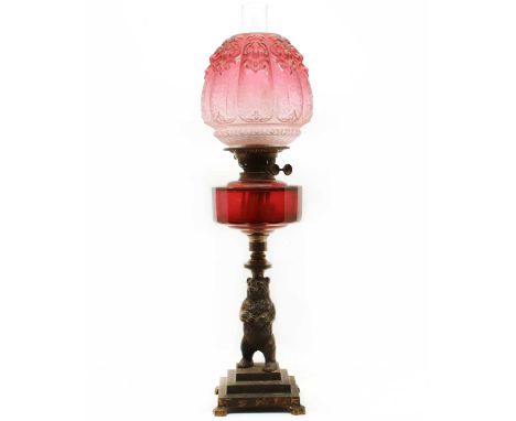 A Victorian metal bear oil lamp, with a cranberry reservoir and an etched and moulded pink shade. 69cm high to top of chimney