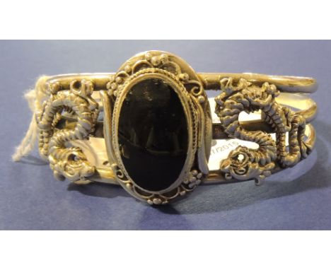 A white metal bangle set with a black hardstone flanked by a pair of dragons.
