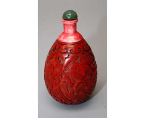 A Chinese cinnabar lacquer snuff bottle with lotus decoration and jade coloured stopper. 8 cms.