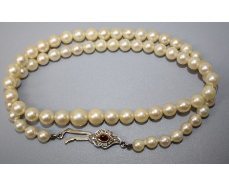 A slightly graduated cultured pearl single row necklace to a cabochon ruby and diamond cluster clasp.47cm length. Largest pea
