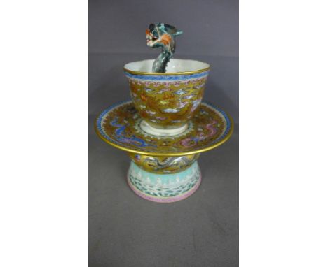 A Chinese Magic cup and stand, lavishly decorated in famille rose enamels and gilt, Qianlong seal mark but 20th century fitte