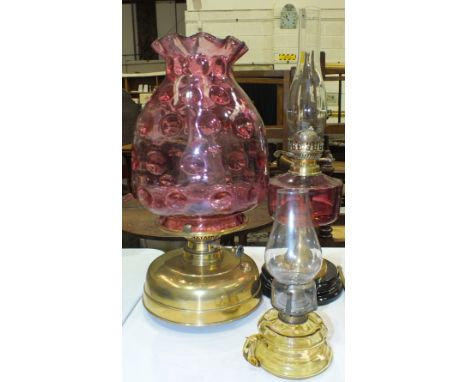 A reproduction oil lamp with cranberry glass reservoir and brass column on ceramic plinth, a modern brassed oil lamp with cra