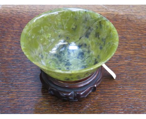 A CHINESE CARVED JADE BOWL, ENGRAVED NUMBERS TO BASE, 10cm DIAMETER RAISED ON CARVED HARDWOOD STAND BEARING OLD COLLECTION LA