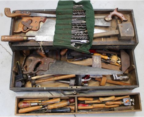 A vintage black painted toolbox containing vintage tools to include a bit and brace, various saws, a spirit level etc.