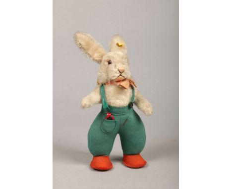 A Steiff Original mo hair rabbit. Wearing a bow tie, with green felt dungarees and orange shoes, 25cm.