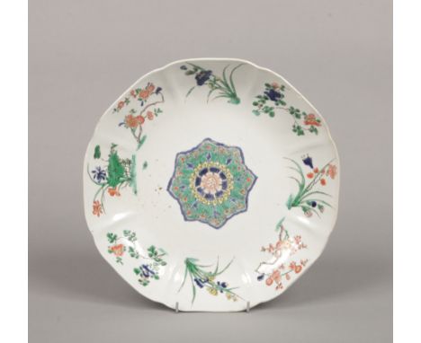 A Chinese Kangxi (1662-1722) scalloped famille verte dish. Painted with flower specimens to each flute and with a central man