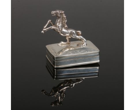 A silver trinket box with hinged cover. Surmounted with a cast silver model of a rearing horse and with an engraved border. A