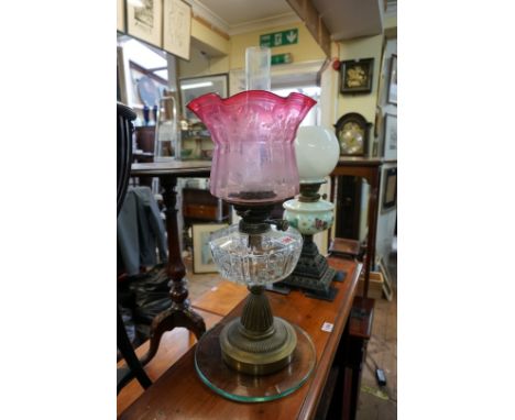 A brass and glass oil lamp, with etched cranberry shade, height excluding chimney 50.5cm high; together with another Victoria