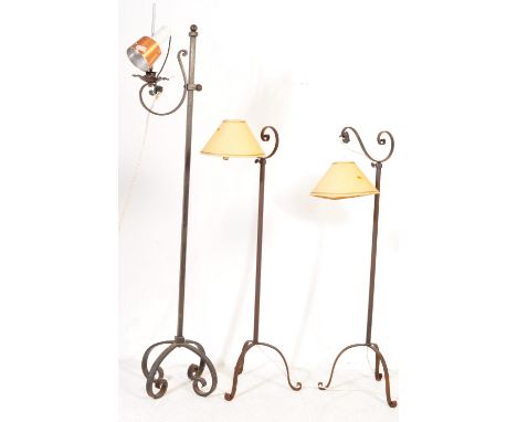 A collection of three wrought iron standard lamps / floor lights comprising of a pair with paper shades and one with adjustab