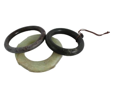Three Jade Bangles The first a flattened pale green example with allover white flecks, the second, a brown and white calcifie