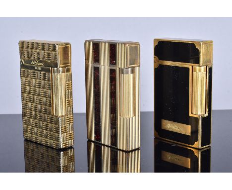Three reproduction Dupont yellow metal pocket lighters, one with engine turned design, one with black lacquered panels, the o