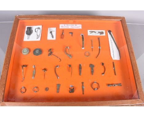 A collection of Roman Bronze items in well presented display, including a coin, tweezers, rings, and various other items 