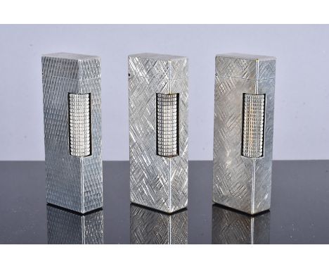 Three Dunhill white metal pocket lighters, two with engine turned design, the other with repetitive geometric design, both st