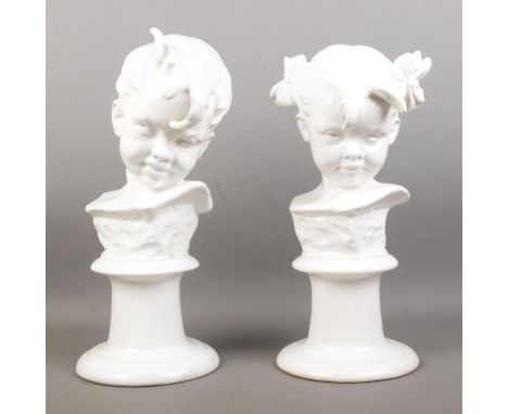A pair of white glazed ceramic busts, depicting a boy and girl. Raised on turned stepped bases. Height: 33cm.  Slight chips t