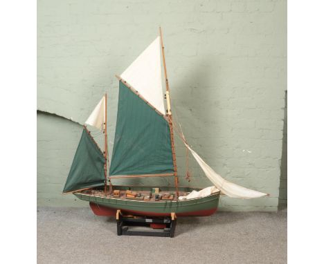 A large remote control model fishing boat with green and white cloth sails on display stand. Approx. length 154cm height 159c