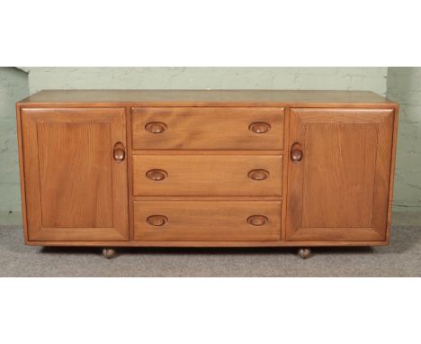 An Ercol light elm Windsor sideboard with three drawers flanked by cupboard doors. The top drawer bearing cutlery compartment