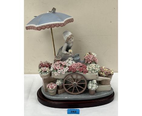 A Lladro figure, 'Flowers of the Season', modelled as a flower girl with cart and baskets profusely decorated with encrusted 