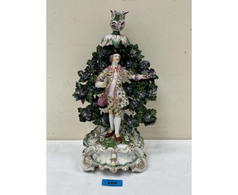 An 18th Century Chelsea candlestick, modelled as a gaily clad figure standing against bocage. Gold anchor mark. 12" high. Dam