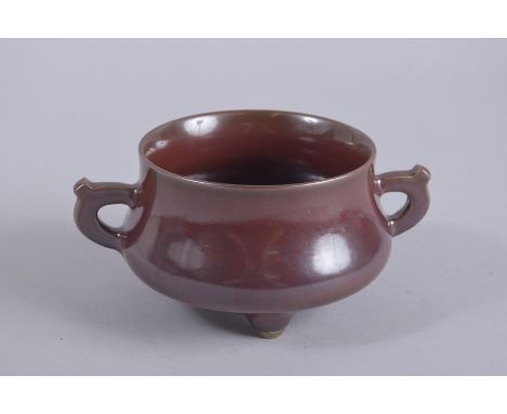 A CHINESE OX BLOOD TWIN HANDLE TRIPOD CENSER, base with character mark, 17cm wide handle to handle.