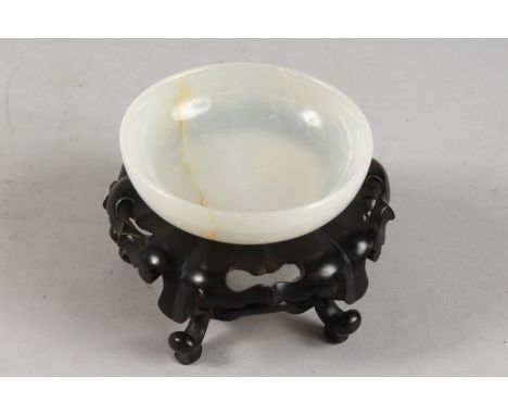 A CHINESE WHITE JADE BOWL ON HARDWOOD STAND, with applied collection sticker to base, bowl 9.5cm diameter.