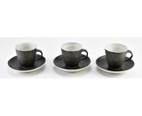 † LUCIE RIE (1902-1995); a trio of stoneware cups and saucers partially covered in manganese with sgraffito decoration, impre