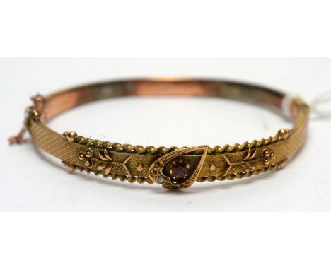 A 9ct yellow gold buckle pattern bangle, set with red stone and seed pearls (missing some), 6.6g gross. 