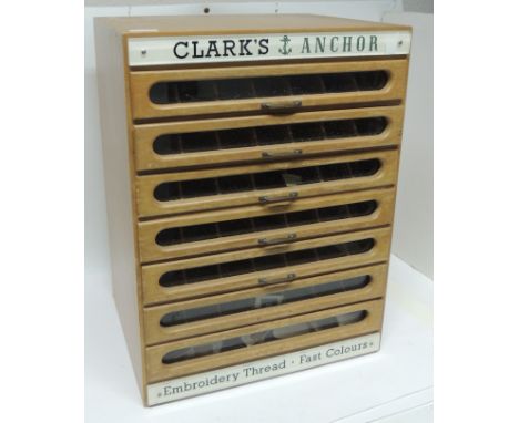 A shop cabinet for Clarke's Anchor Embroidery Thread, the light wood cabinet with seven narrow glass fronted drawers, each dr