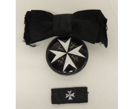 An Order of St John breast badge, circular white metal with raised white enamel Maltese cross and white metal animals, on bla
