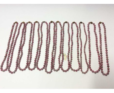 Collection of twelve Chinese pink hard stone necklaces with round polished beads and oval silver gilt clasps with wire work f