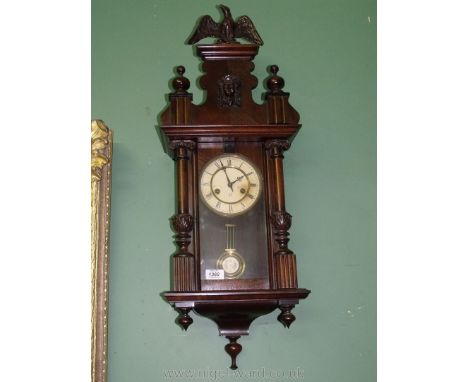 A dark wood cased wall clock with an eagle pediment and Acanthus leaf detail to the Roman style pillars that enclose the glas