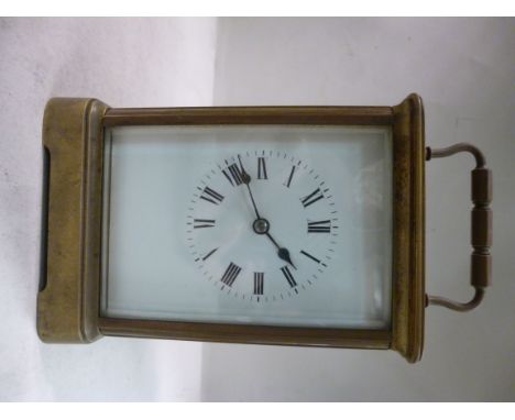 An early 20thC lacquered brass cased carriage clock with bevelled glass panels and a folding top handle, on a bracket plinth;