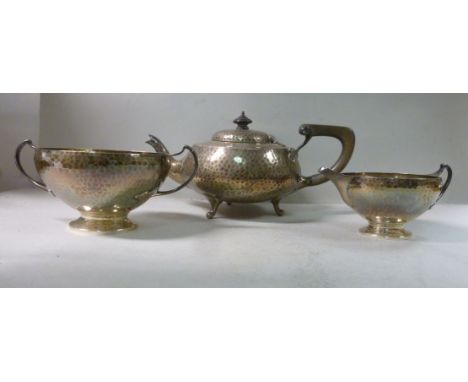 A matched three piece, spot-hammered silver tea set comprising a teapot of squat, bulbous form with an insulated handgrip, kn