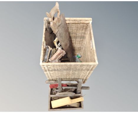 A wicker lidded basket containing vintage hand saws together with further wooden caddy containing hand tools 