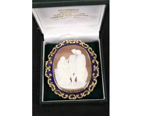 A large yellow metal cameo brooch with blue enamel and scroll work border, the central cameo decorated with classical scene