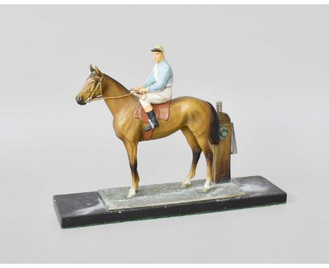 A Cold Painted Spelter Table Lighter, in the form of a racehorse with jockey up, complete with striker, raised on a rectangul