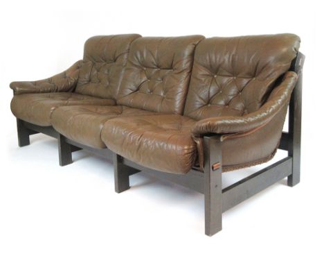 A 1970's three seater sofa, the green button upholstered cushions on a slung seat with hardwood frame and buckled reverse, in