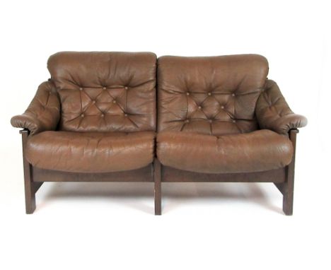 A 1970's two seater sofa, the brown button upholstered cushions on a slung seat with hardwood frame and buckled reverse, in t