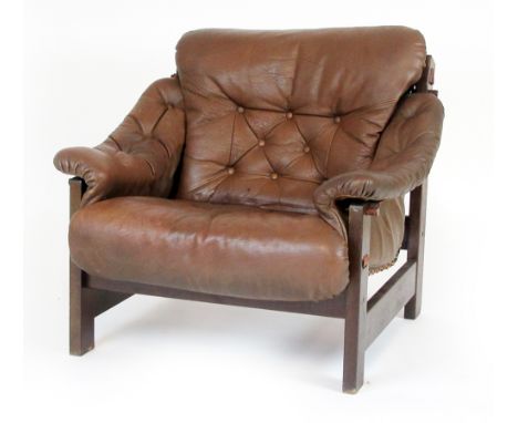 A 1970's armchair, the brown button upholstered cushion on a slung seat with hardwood frame and buckled reverse, in the manne