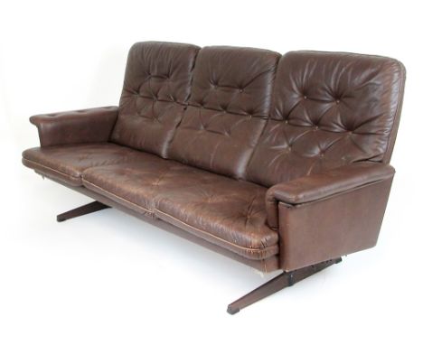 A 1970's brown button upholstered three seater sofa on black and faux rosewood supports CONDITION REPORT: Structurally sound,