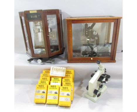 A microscope in a glass isolation chamber, a mid 20th century laboratory microscope and a set of Chemist’s scales in a glass 