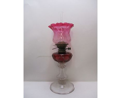 A late Victorian cranberry and clear glass oil lamp with a brass burner, on acanthus decorated bowl, wrythen column and foldo