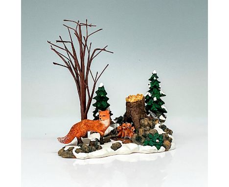 Department 56 figurine depicting a fox and its offspring in a snowy wilderness as well as forest trees and shrubbery. This it