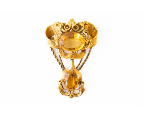 A CITRINE BROOCHSet with an oval cut citrine in an ornate surround, suspending a further oval cut citrine from a rope chain, 