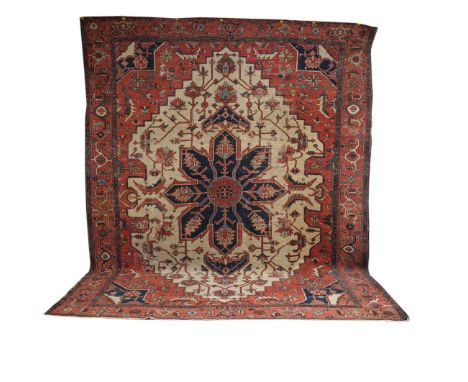 AN HERIZ CARPET, PERSIANThe ivory shaped field within an outer madder surround, a bold dark indigo flower medallion, indigo s