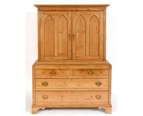 A stripped pine cabinet on chest, having a pair of lancet panel doors, above two short and two long drawers, on bracket feet,