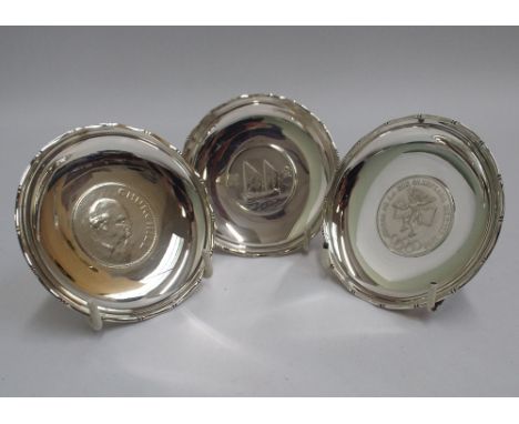 Three small silver circular dishes, each inset with a coin, stamped Sterling Silver Made in Hong Kong to the backs.  8.5cm in