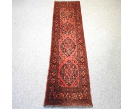 An Afghan woollen runner, with three central medallions, on a red ground, 291 x 77cm