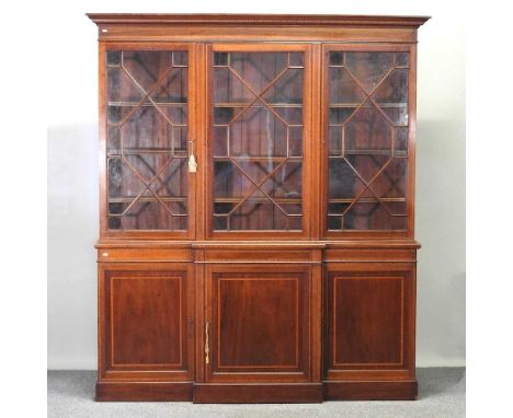 An Edwardian mahogany and satinwood banded breakfront library bookcase, with astragal glazed doors, over panelled doors, on a